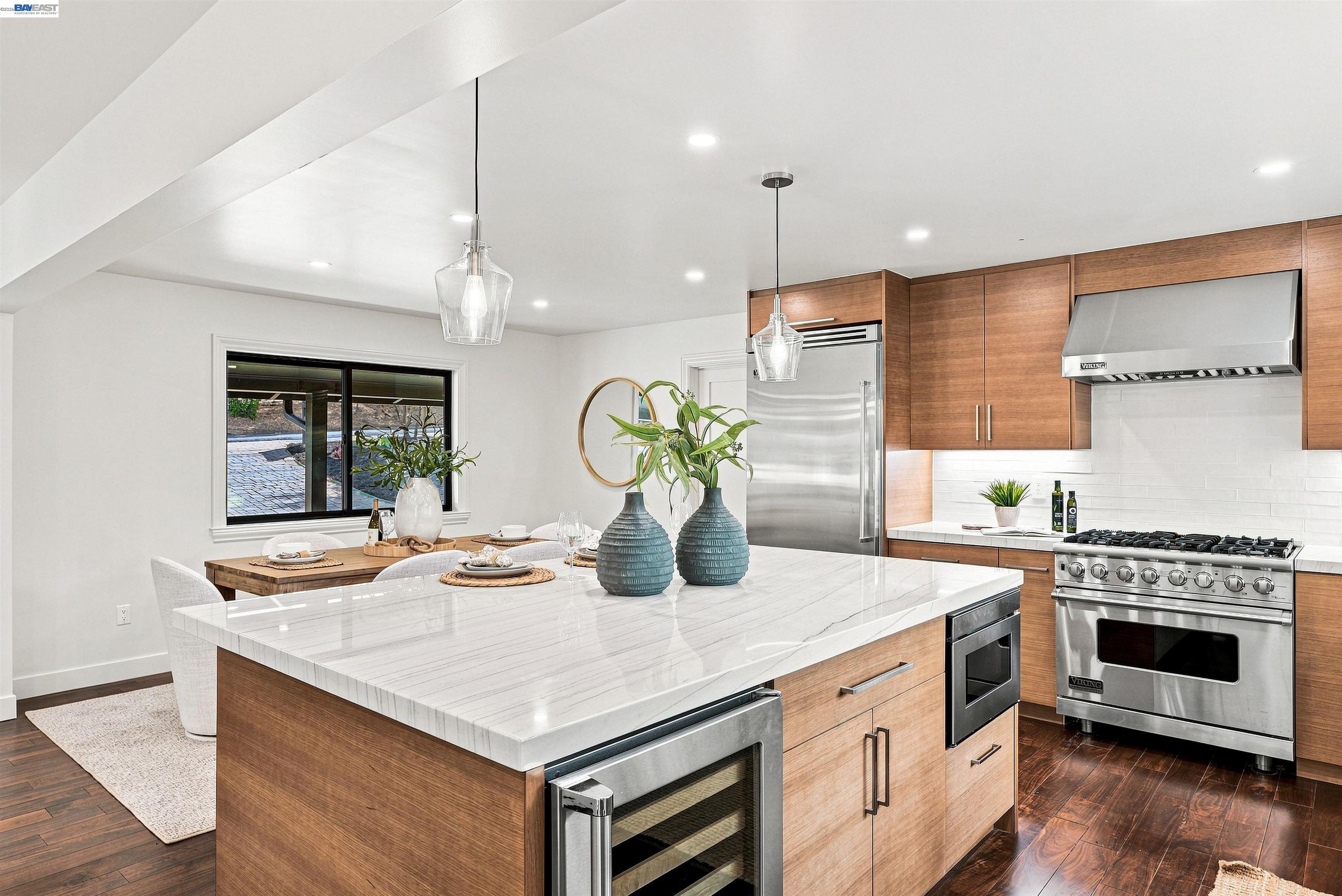 Staged kitchen with a marble island, wood cabinetry, stainless steel appliances, and adjoining dining area.