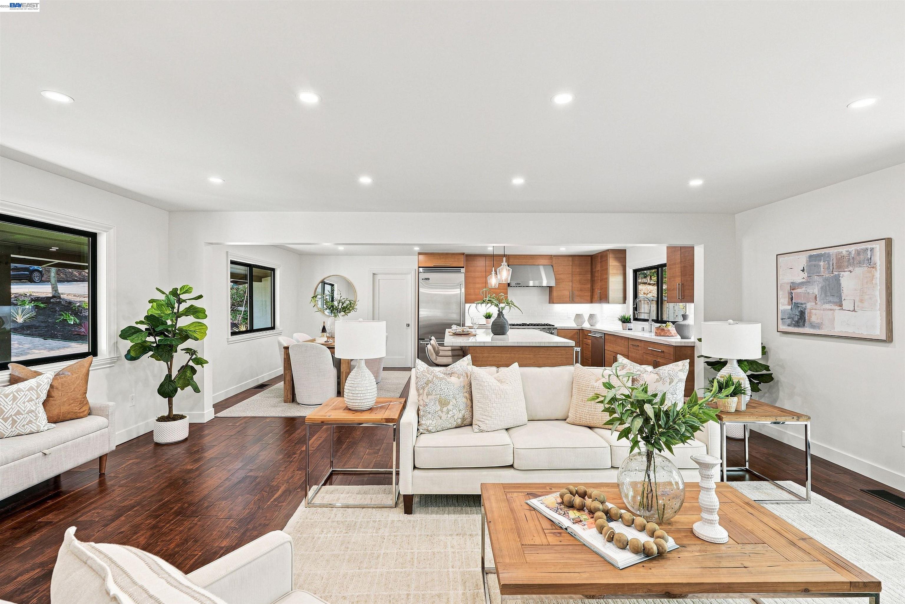 Open-plan living room and kitchen with cream seating, dark hardwood floors, and warm wood cabinetry.
