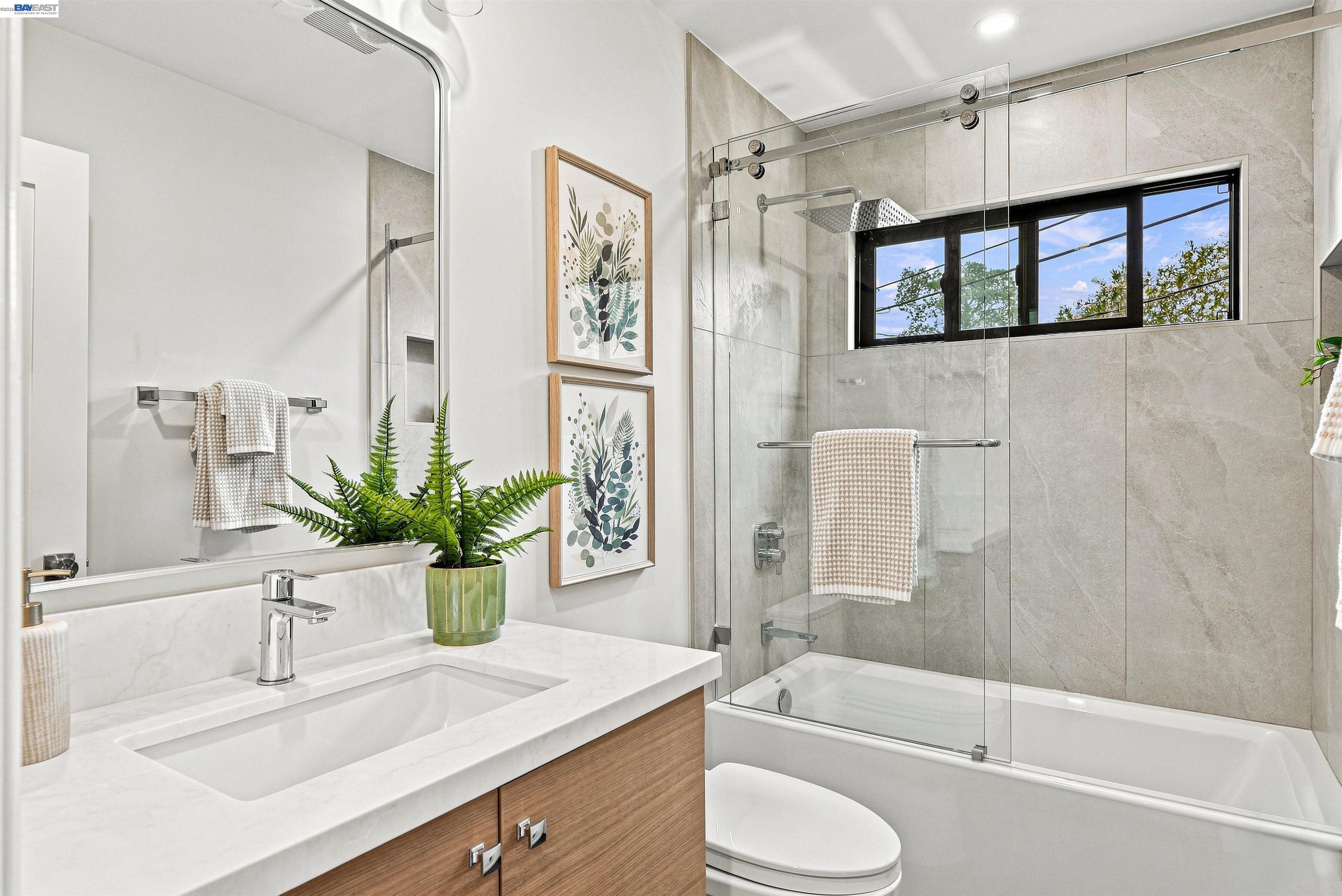 Staged bathroom with a wood vanity, glass shower, bathtub, and wide window.