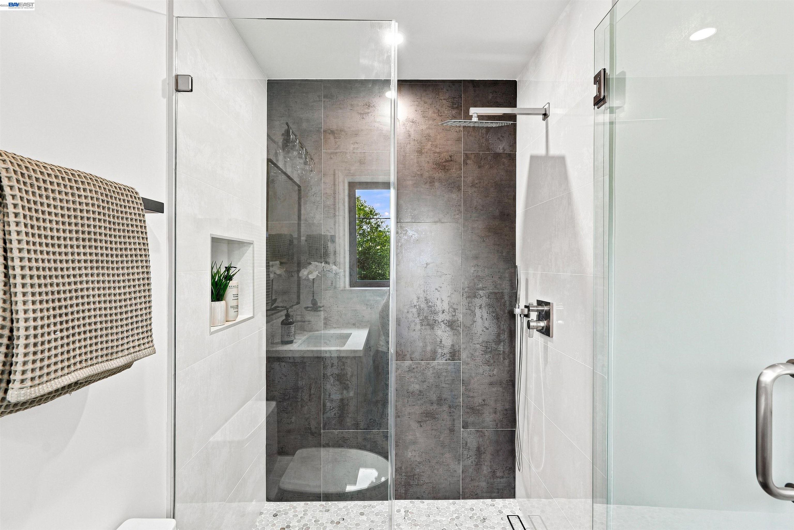 Glass-enclosed walk-in shower with dark tile, rainfall showerhead, and pebble floor.
