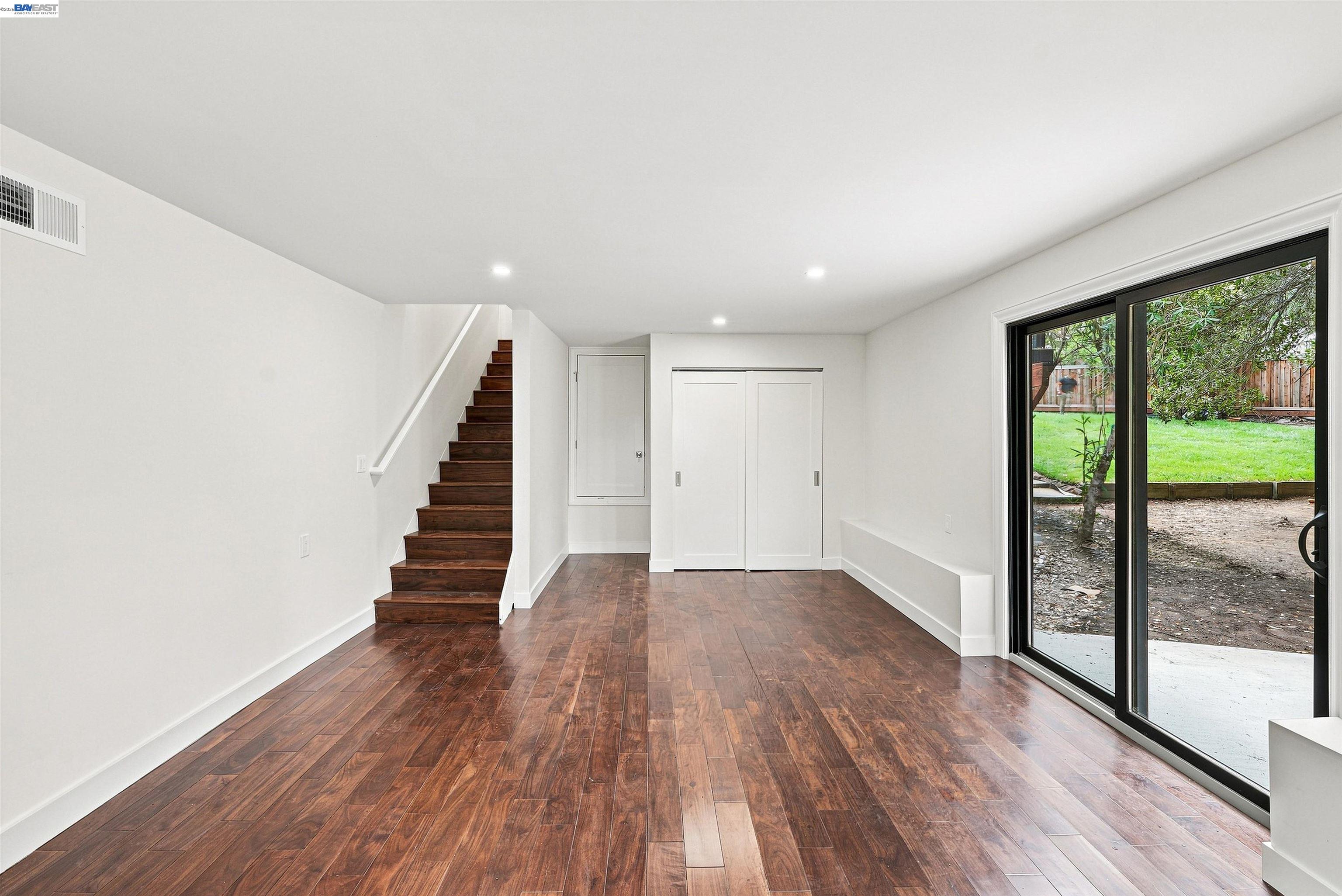 Empty room with dark hardwood floors, a staircase, and sliding glass doors to the backyard.