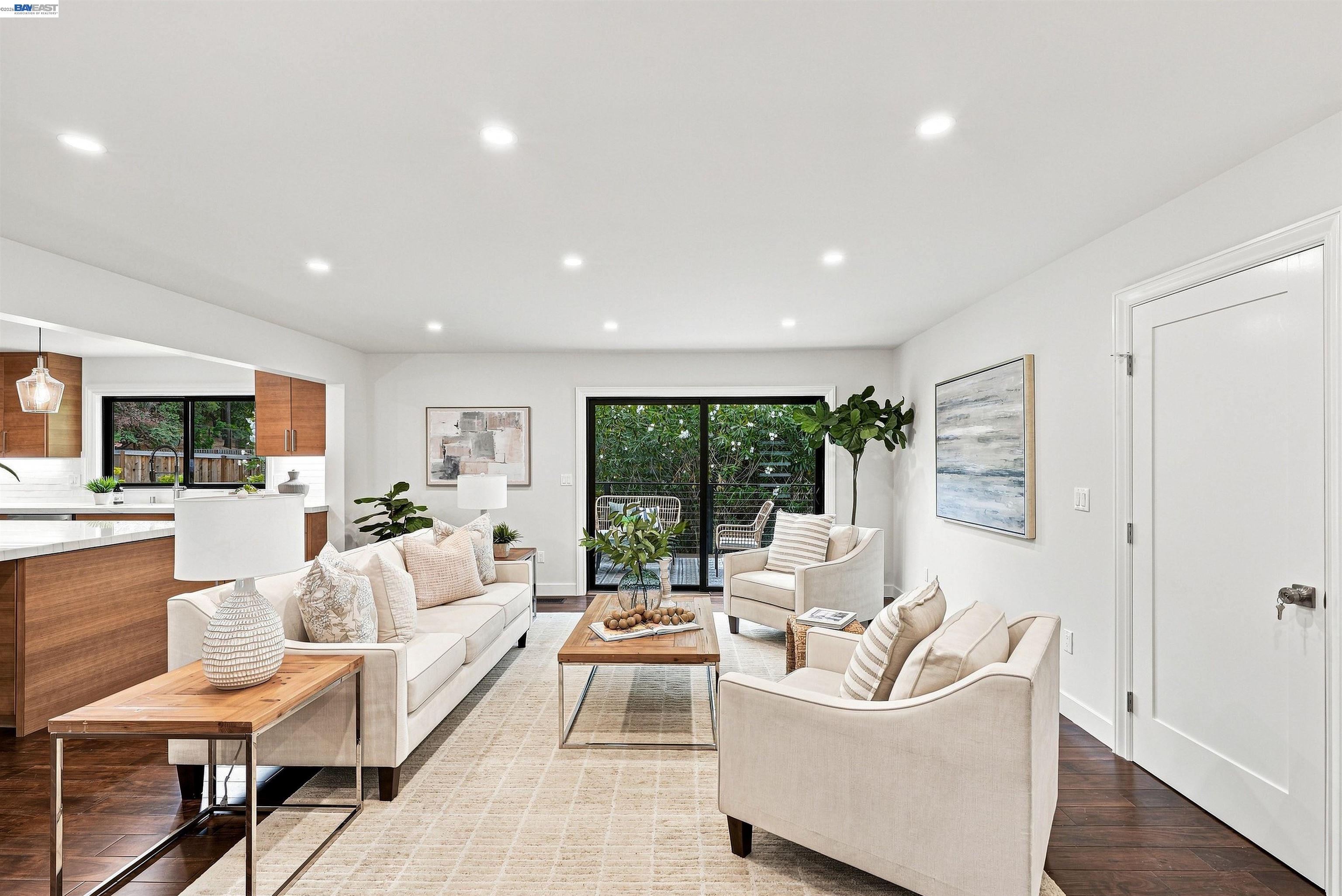 Staged living room with cream seating, dark wood floors, and sliding glass doors to greenery.