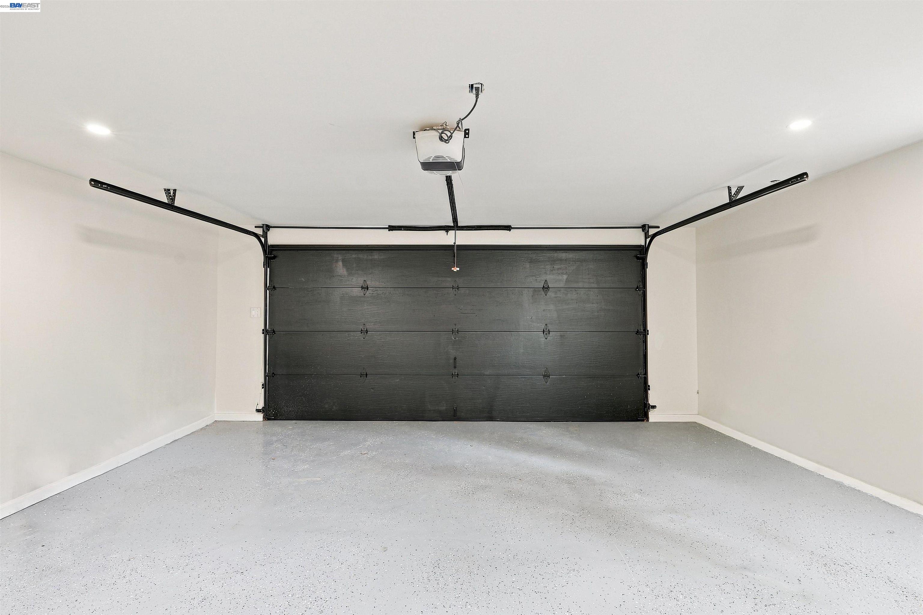 Empty garage with a black sectional door and light gray speckled floor.