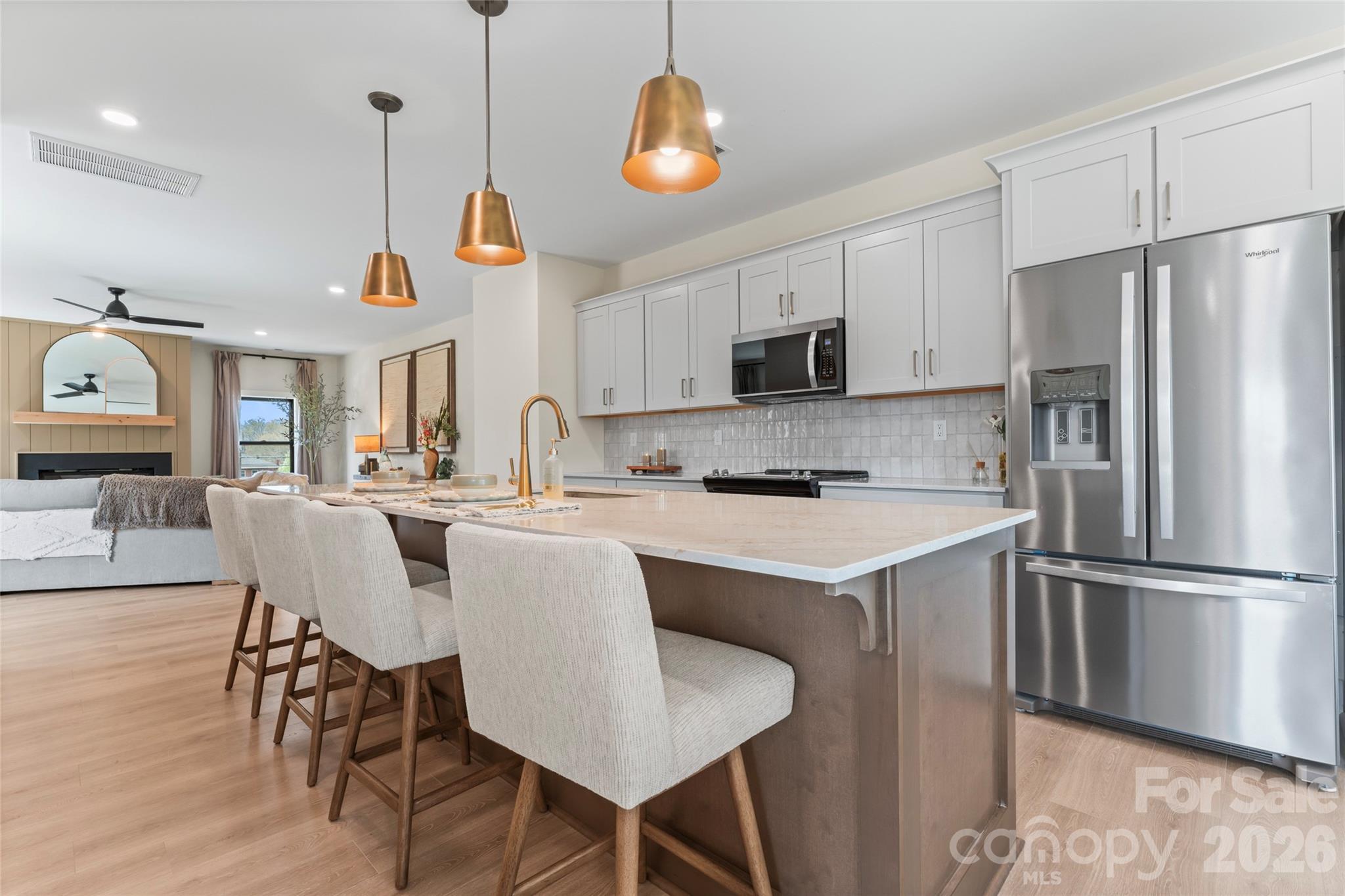Open kitchen with a large island and seating, white cabinetry, and a living area with a fireplace.