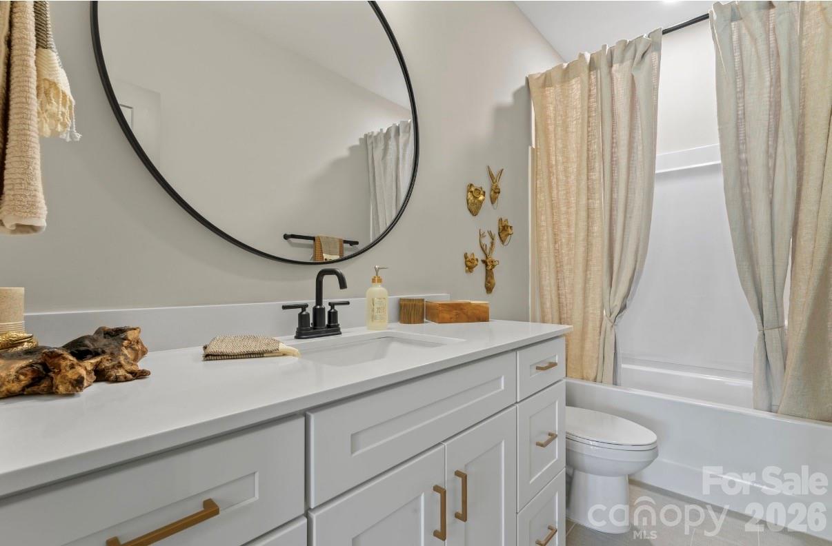 Bathroom with a white vanity, round mirror, and curtained bathtub beside a toilet.
