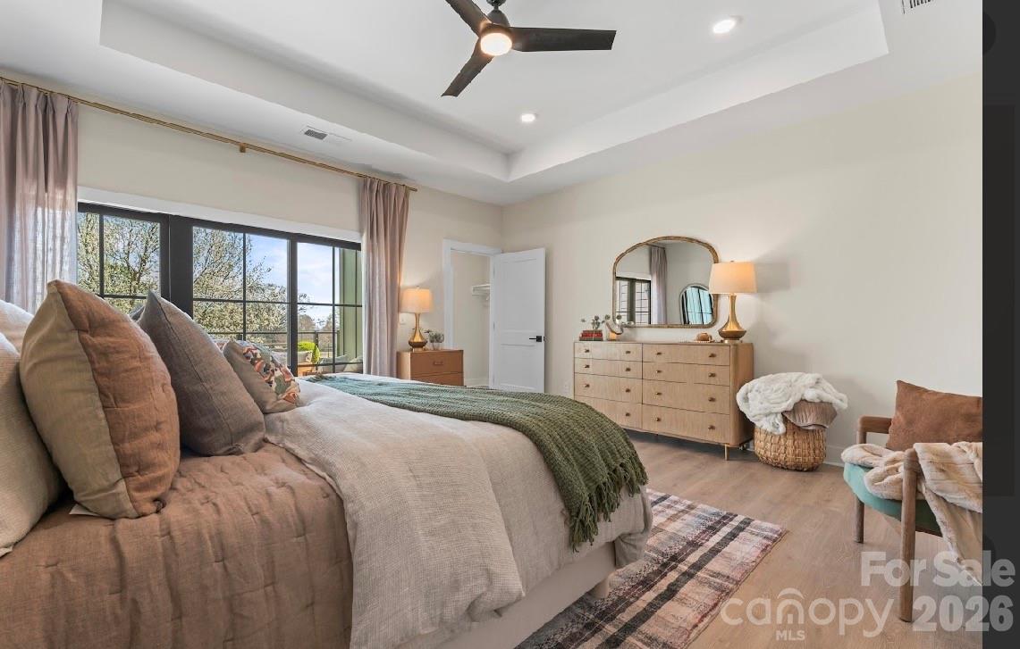 Furnished bedroom with a large bed, green throw, black-framed windows, and wood dresser.