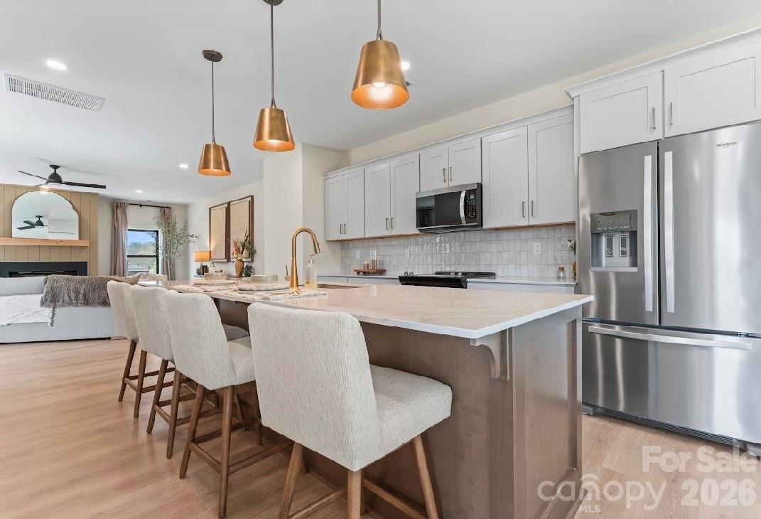 Open kitchen with white cabinets, stainless steel appliances, and a large island with seating beside the living area.