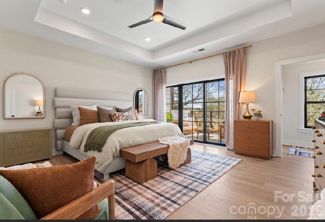 Staged bedroom with a king bed, plaid rug, ceiling fan, and sliding doors to a balcony.