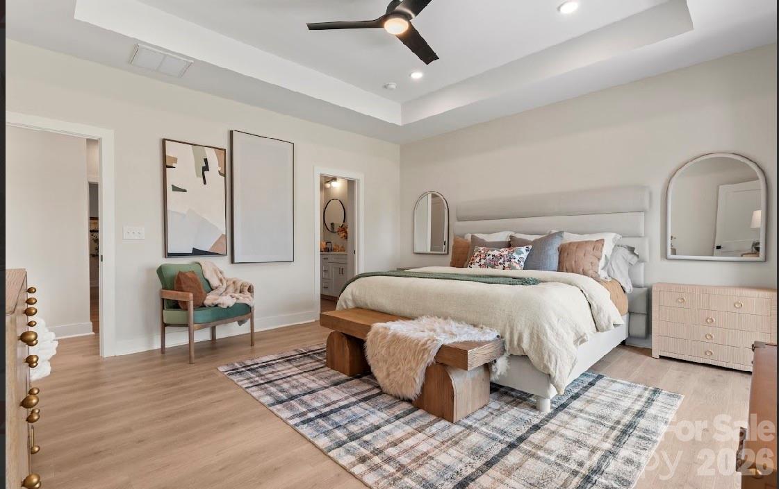 Staged bedroom with a large upholstered bed, plaid rug, wood bench, and green accent chair.