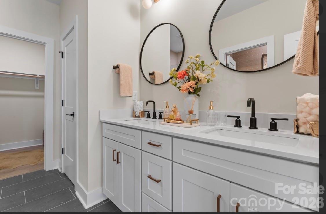 Bathroom with a long double vanity, black faucets, round mirrors, and an open closet doorway.