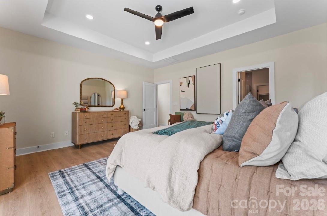 Staged bedroom with a tray ceiling, dark ceiling fan, wood dresser, and arched mirror.