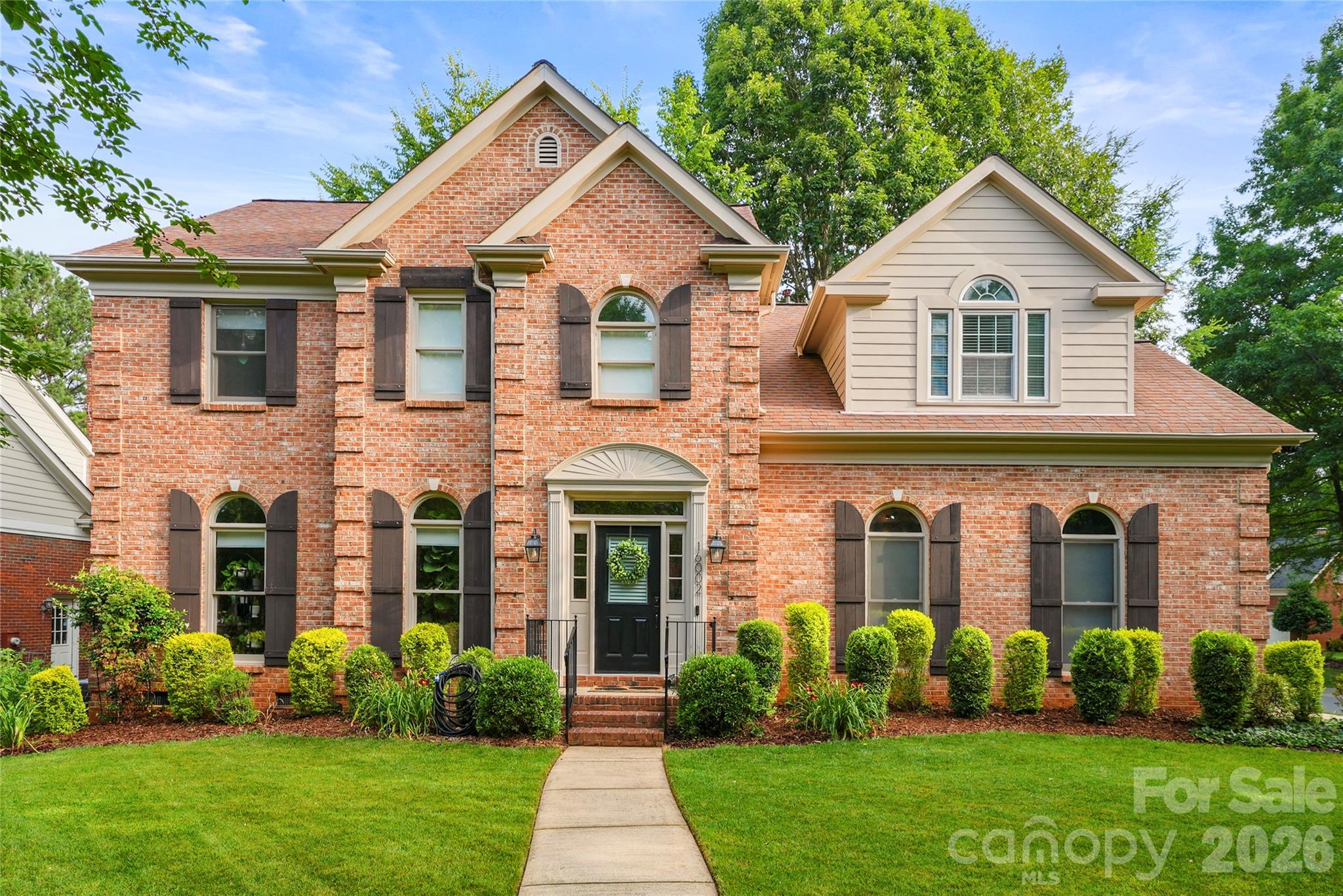 Two-story brick house with arched windows, dark shutters, and a landscaped front lawn.