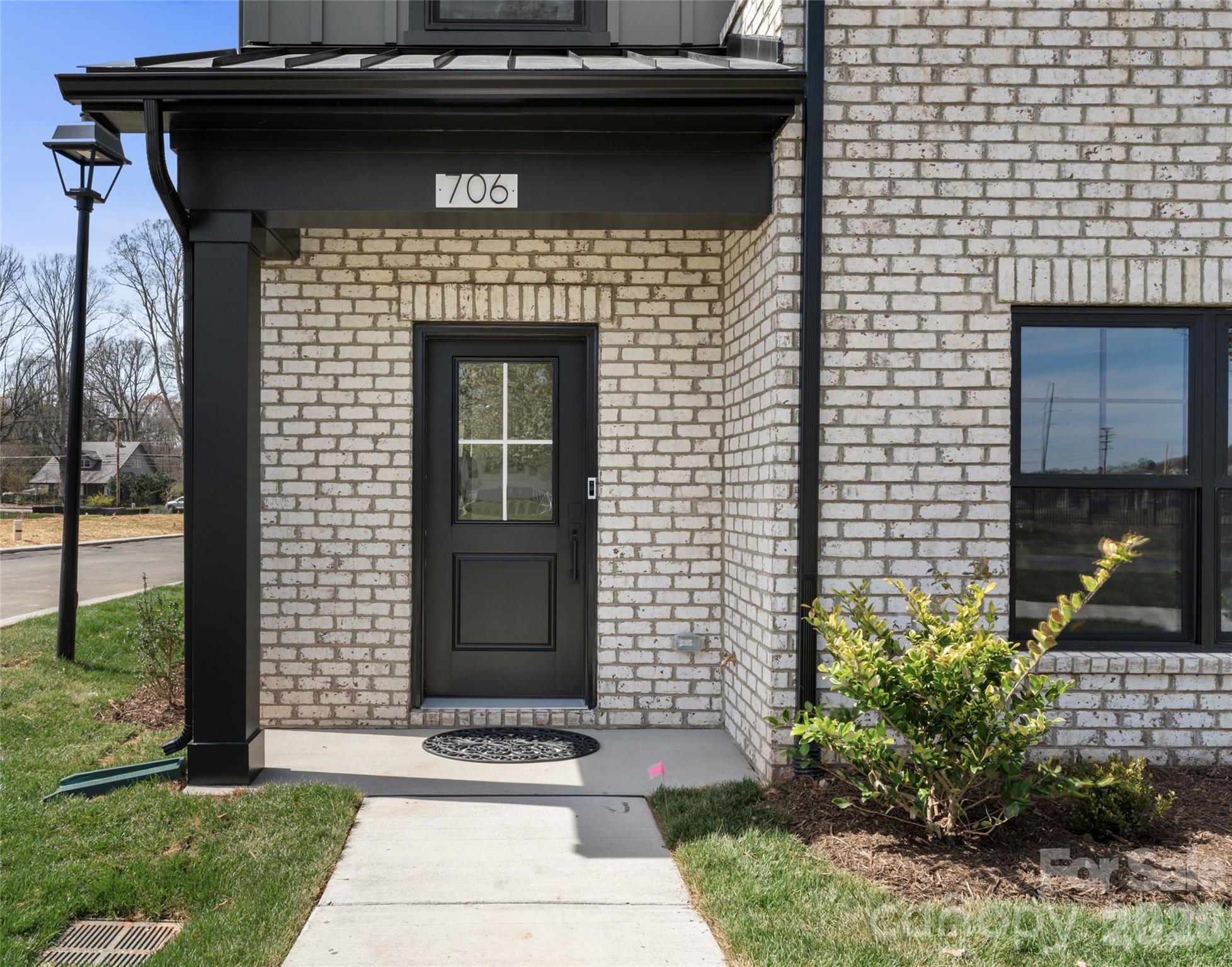 White-brick home entrance with a black door, covered porch, and concrete walkway.