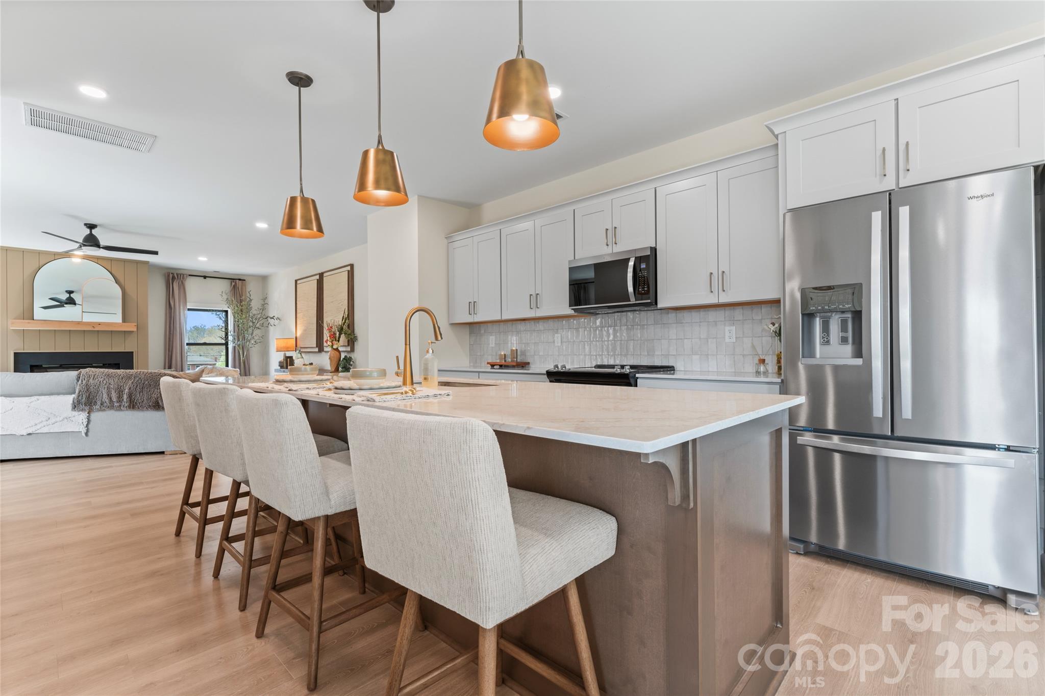 Open-plan kitchen with a large stone island, upholstered stools, white cabinets, and stainless steel appliances.