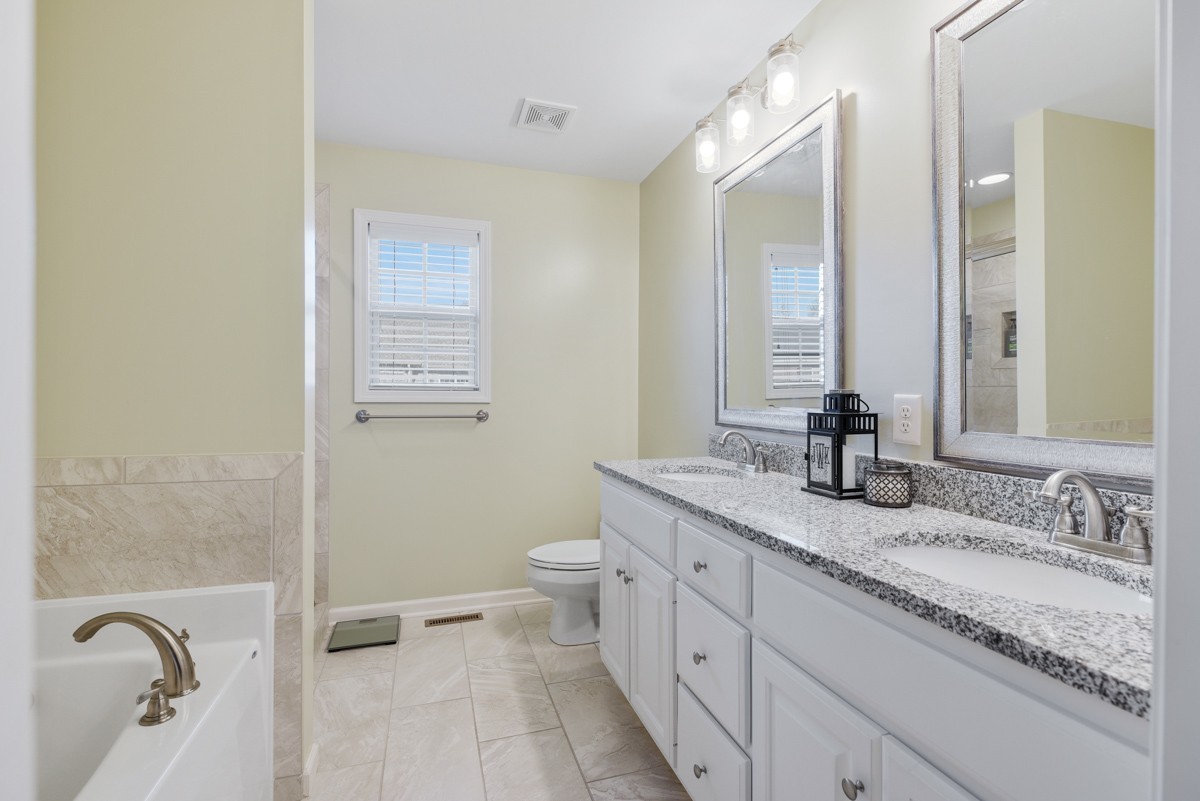 Bathroom with a double white vanity and granite countertop beside a tiled bathtub.