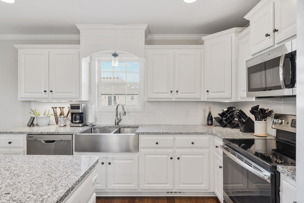 Bright white kitchen with a farmhouse sink, speckled granite counters, and stainless steel appliances.