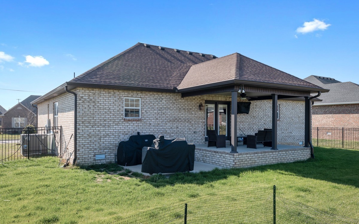 Brick home with a covered patio, outdoor seating, and a grassy fenced backyard.