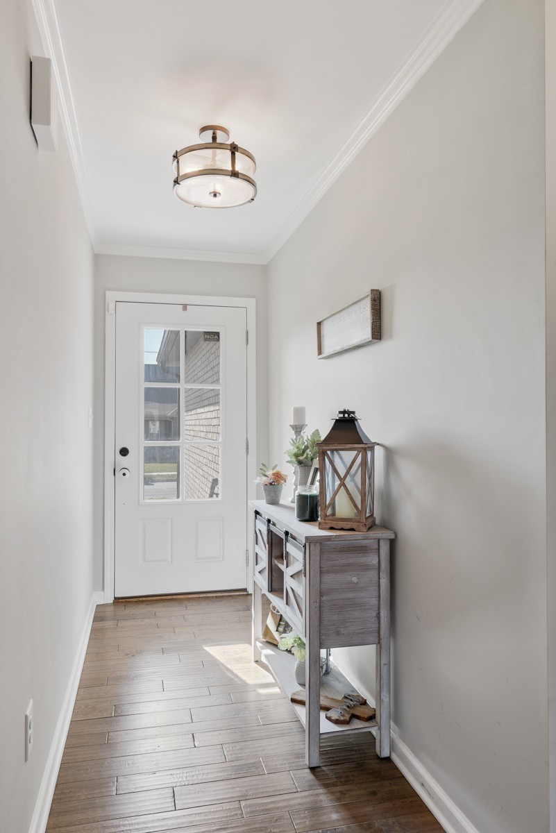 Bright entryway with a glass-paneled front door, wood-look tile, and decorated console table.