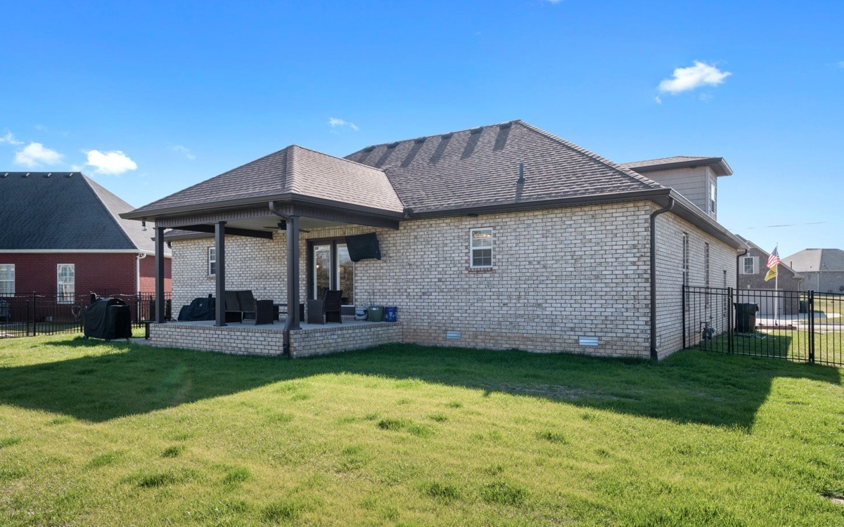 Brick home’s rear exterior with a covered patio and fenced grassy yard.