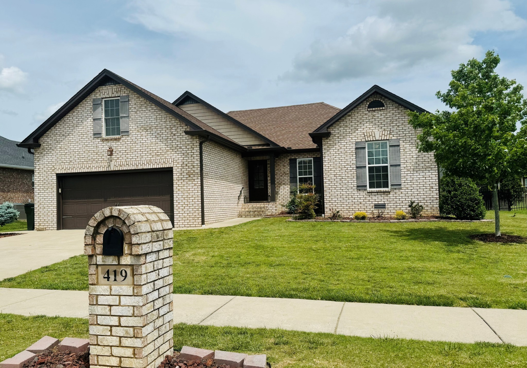 Brick home with a double garage and gabled roof, seen behind a stone mailbox marked 419.