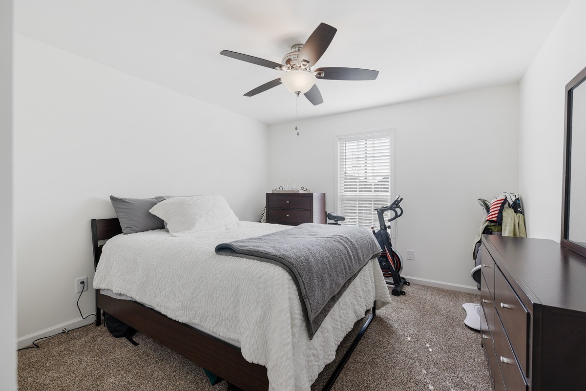 Bedroom with a dark wood bed, white bedding, gray throw, and exercise bike by the window.