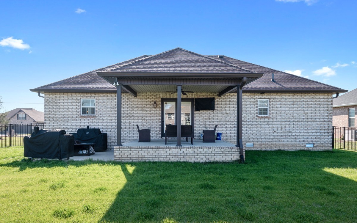 Brick home with a covered rear patio, outdoor seating, grills, and a broad lawn.