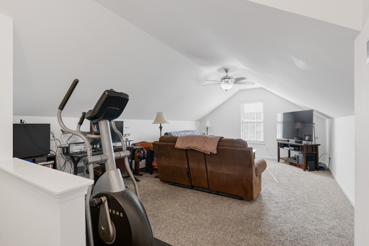 Bonus room with a sloped ceiling, brown sectional, television, and exercise bike.