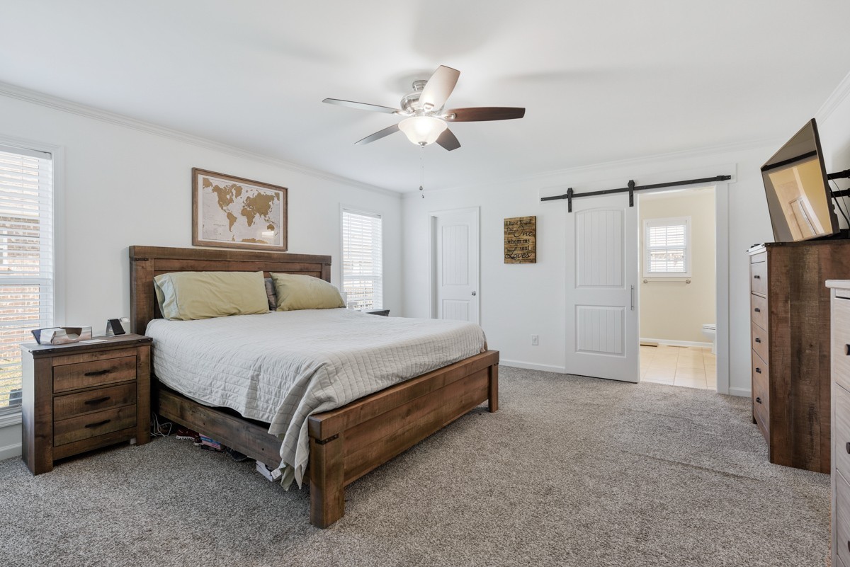 Bedroom with a wooden bed, gray carpet, ceiling fan, and sliding barn door.