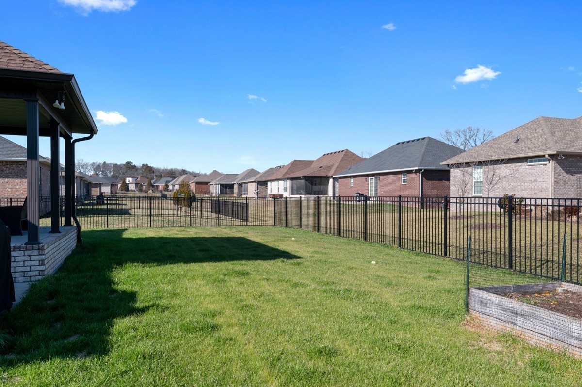 Fenced grassy backyard with a covered patio and neighboring homes beyond.