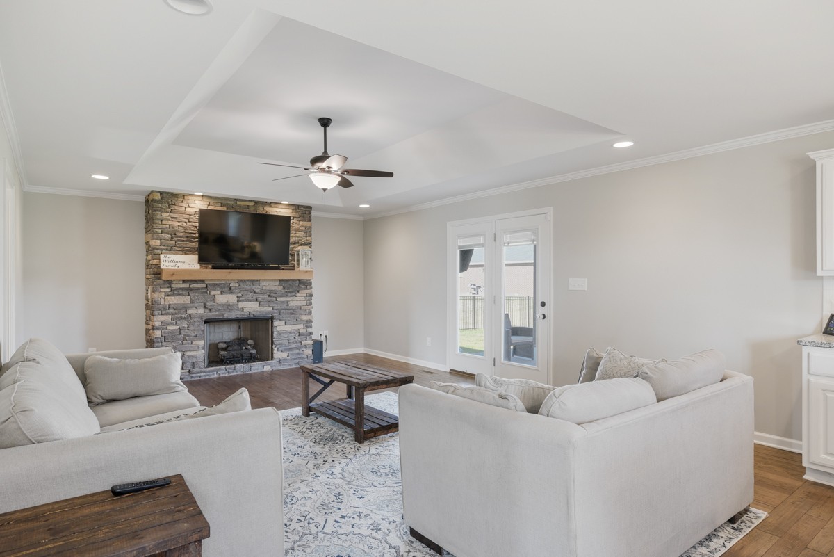 Living room with a stone fireplace, mounted television, light sofas, and tray ceiling.