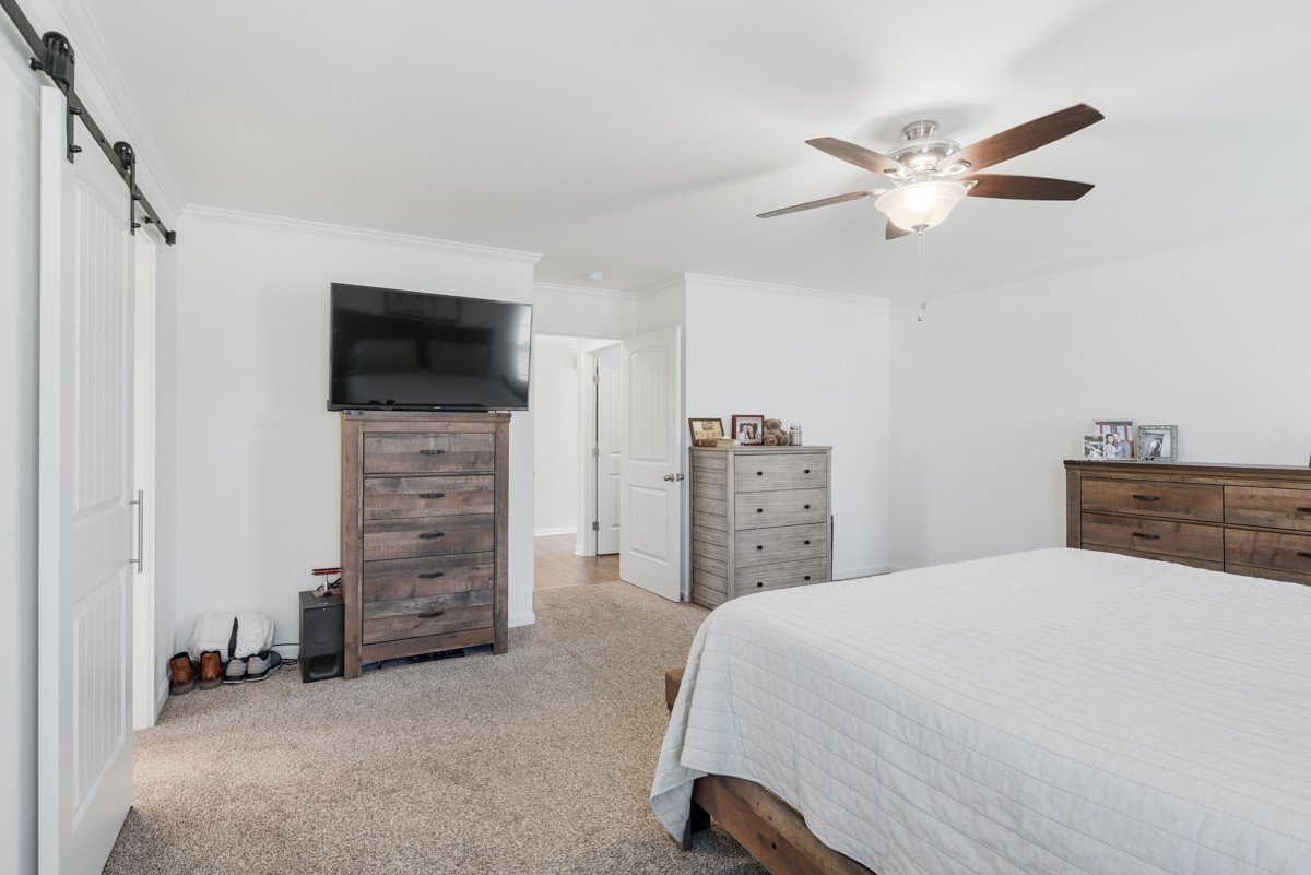 Bedroom with a white-quilted bed, wood dressers, television, and ceiling fan.