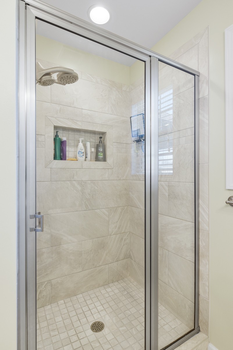 Walk-in shower with beige tile, glass doors, a recessed niche, and a multi-head shower fixture.