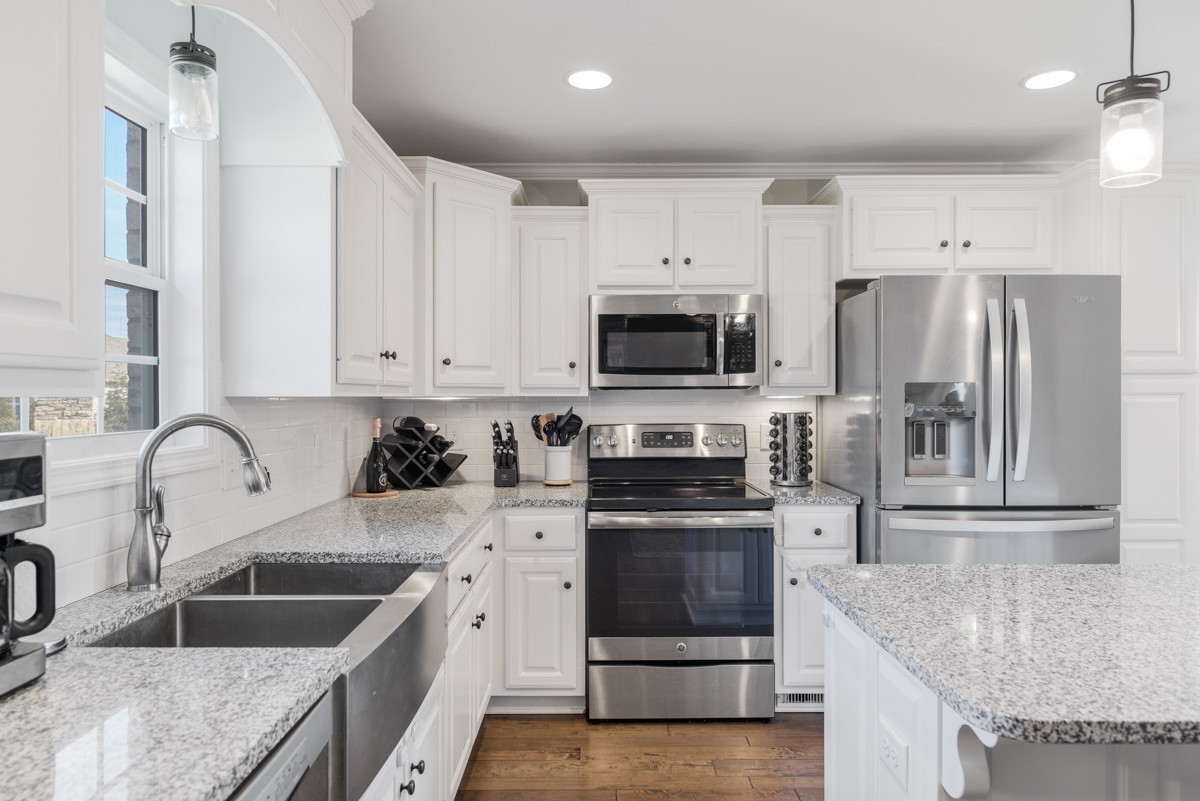Kitchen with white cabinets, granite counters, stainless steel appliances, and a double-basin sink beneath a window.