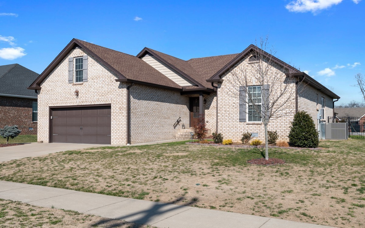 Light-brick home with a two-car garage and broad lawn beneath a clear blue sky.