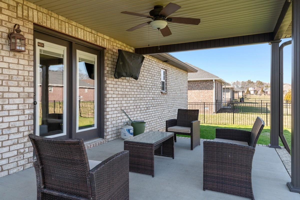 Covered back patio with wicker seating, ceiling fan, and view of fenced backyard.