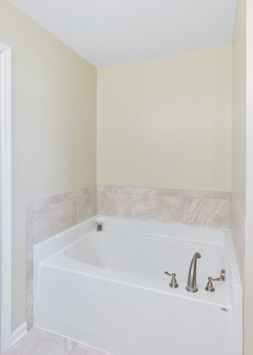 Bathroom with a white soaking tub, marble-look tile surround, and brushed-metal faucet.
