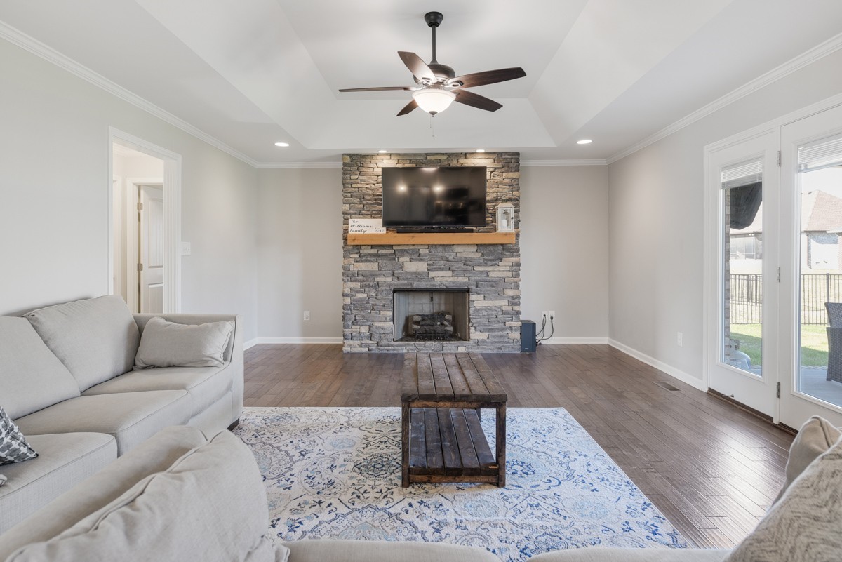 Living room with a stone fireplace, mounted television, tray ceiling, and glass patio doors.