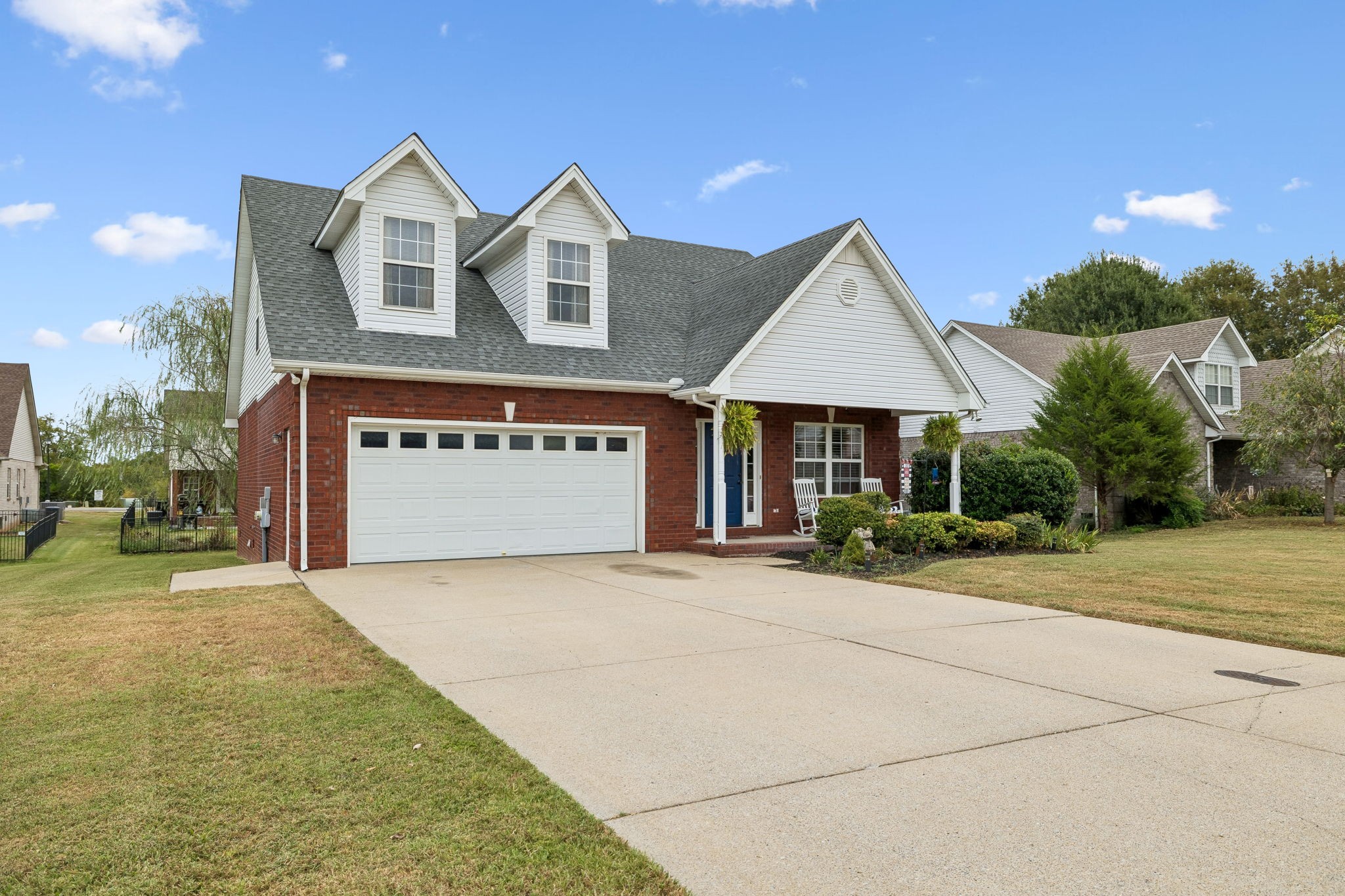 Two-story brick-and-white home with dormers, an attached garage, and a wide concrete driveway.