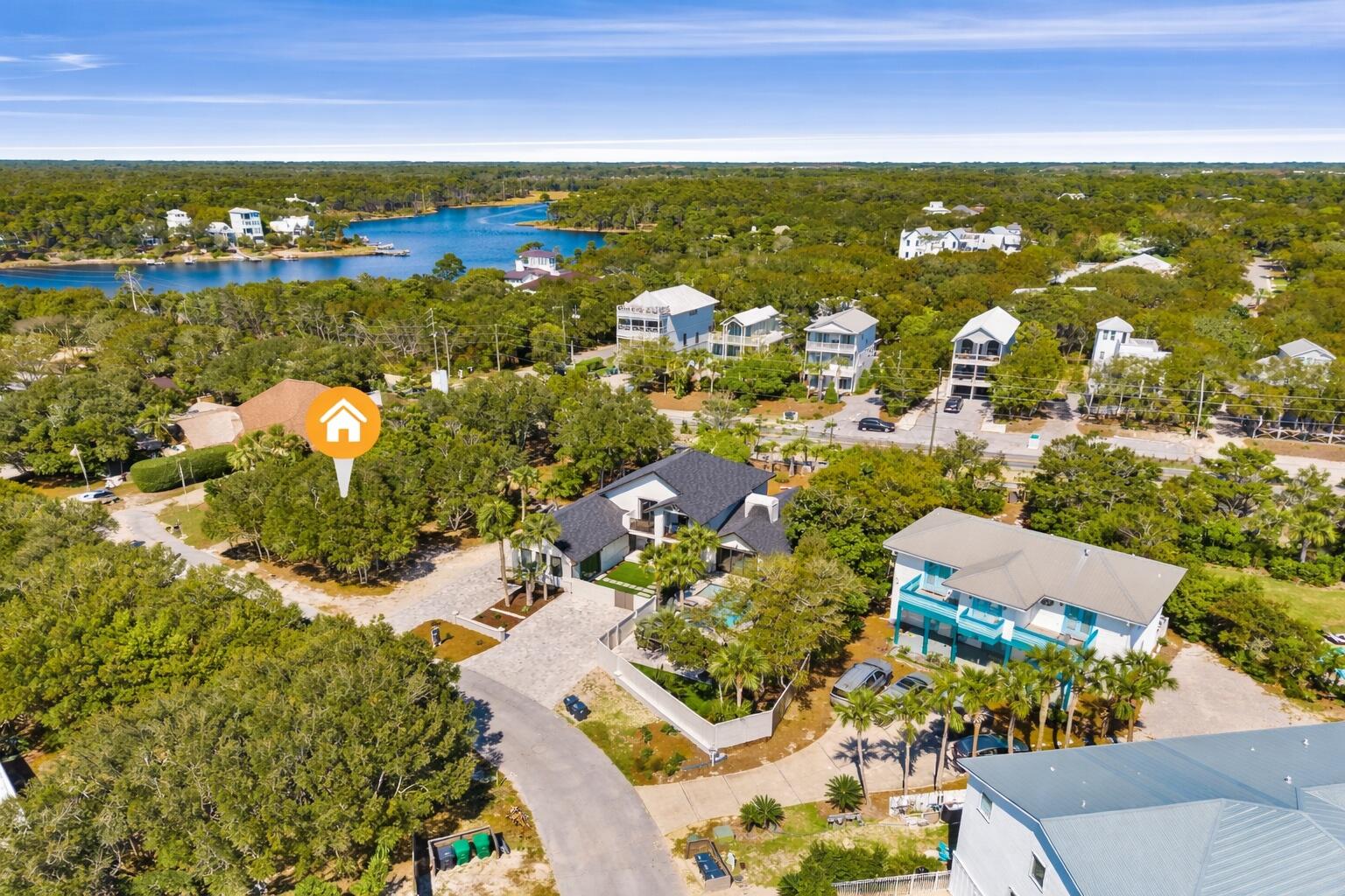 Aerial view of a wooded coastal neighborhood beside a winding waterway, marked with an orange house pin.