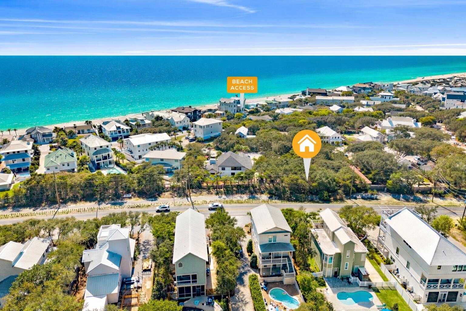 Aerial view of coastal homes beside turquoise water, with a beach access sign and property marker.