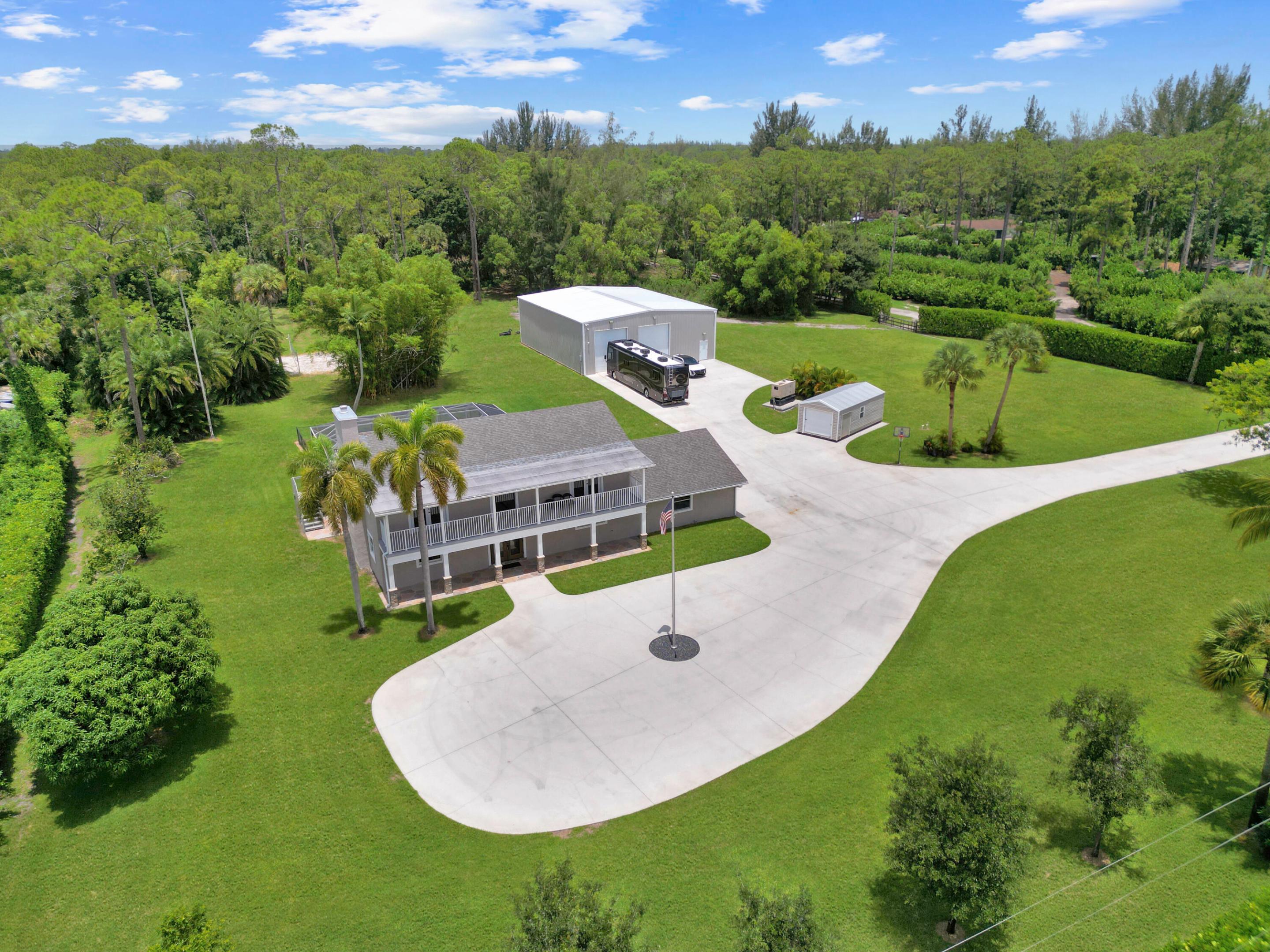 Aerial view of a two-story home with a large outbuilding, motorhome, and curved driveway.