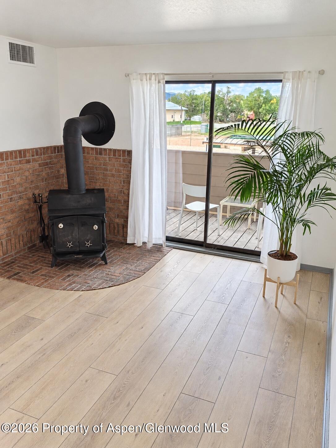 Living area with a black wood stove, brick hearth, light wood floors, and sliding glass door to a deck.