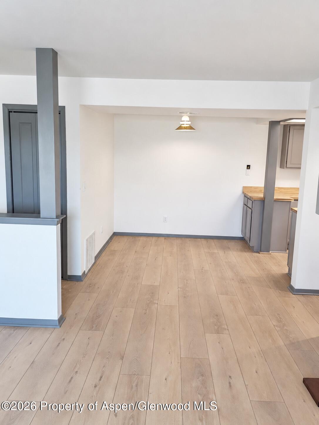 Empty dining area opening to a kitchen, with light wood floors and gray cabinetry.