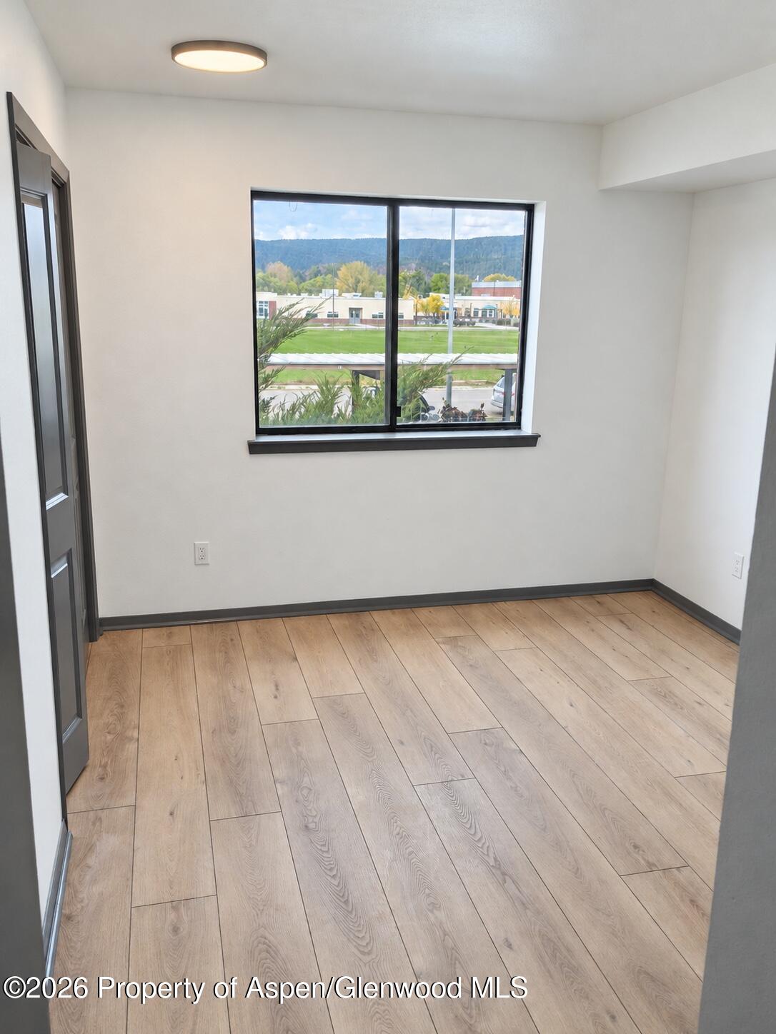 Vacant room with wood-look flooring and a large window overlooking greenery and wooded hills.