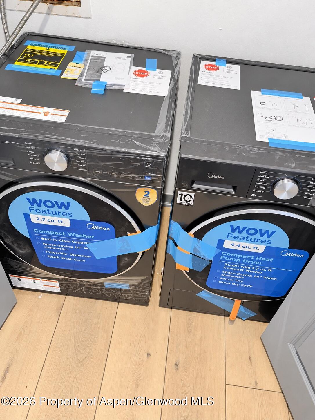 Compact Midea washer and heat pump dryer with blue product labels on light wood flooring.