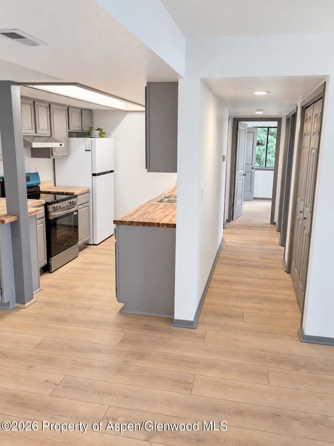 Kitchen and hallway with gray cabinets, butcher-block counters, and light wood-look flooring.