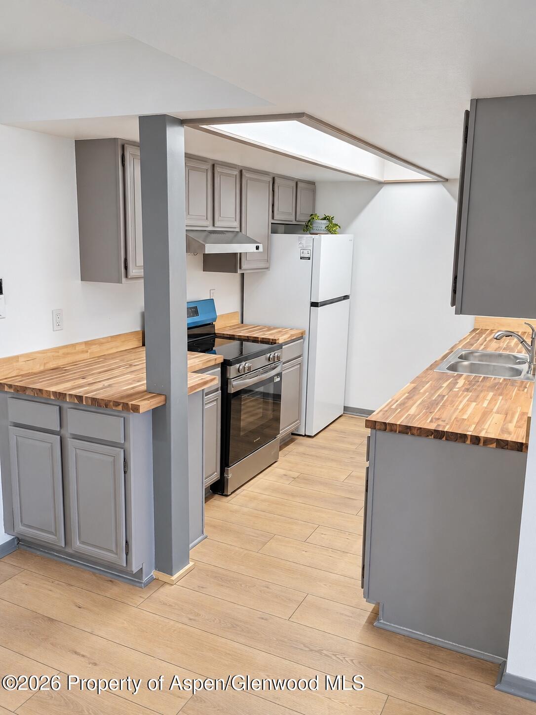 Kitchen with gray cabinets, butcher-block counters, stainless range, and a skylight.