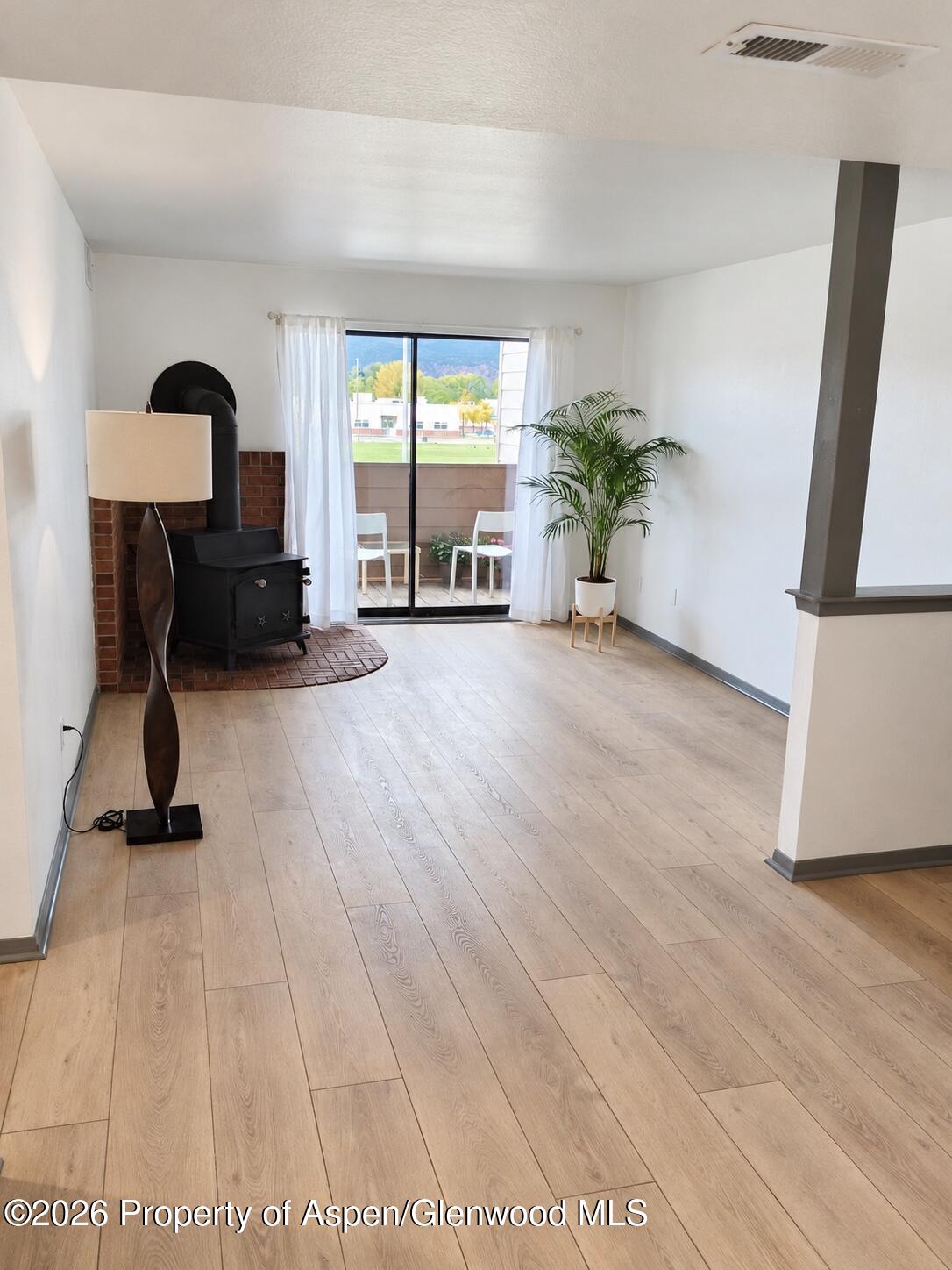 Living room with a black wood stove, wood-look floors, and sliding doors opening to a balcony.