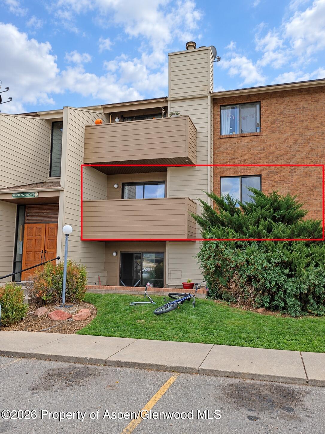 Residential building with a red-outlined unit, balcony, and brick-and-siding facade.