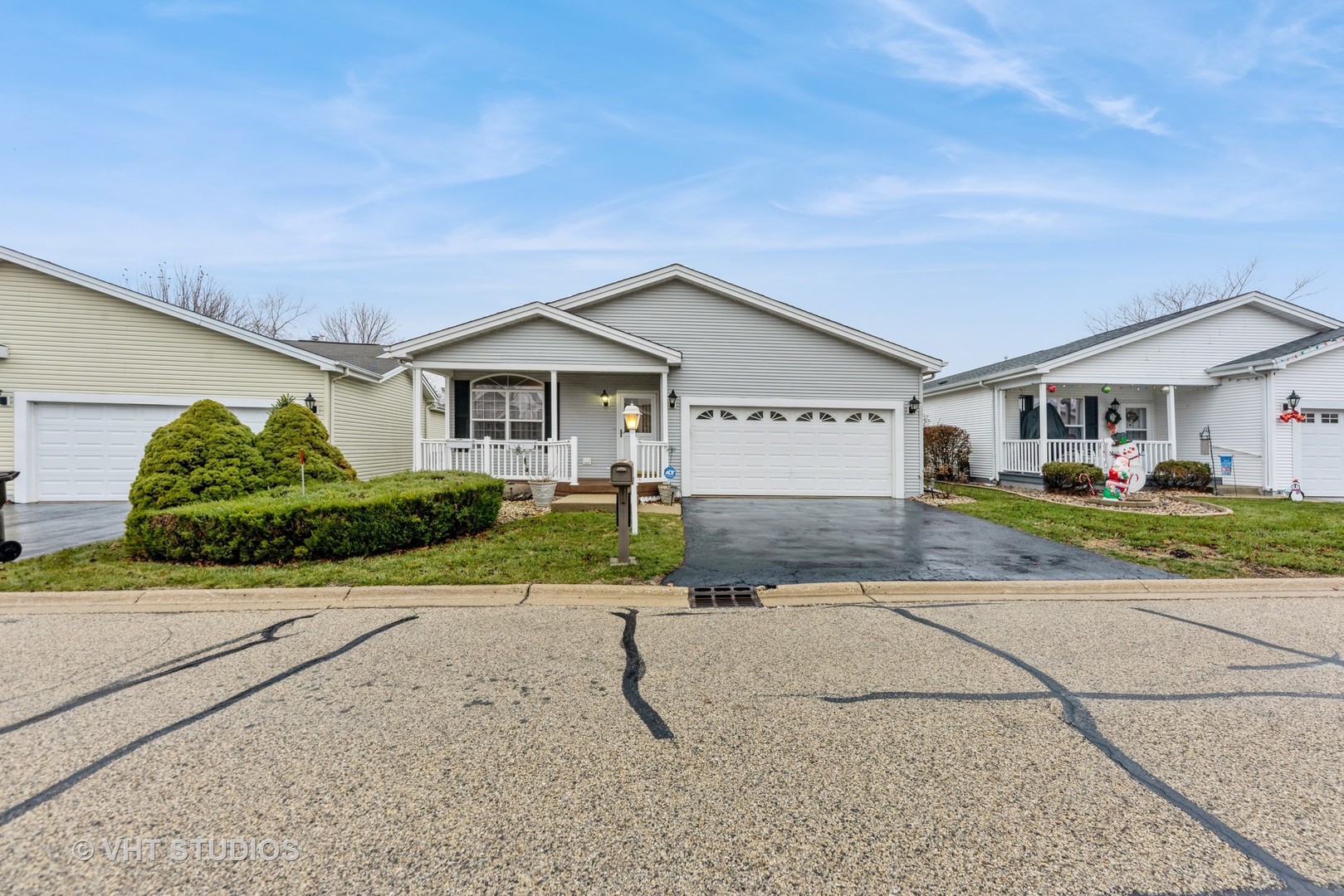 Gray single-story home with an attached two-car garage, covered porch, and trimmed front shrubs.